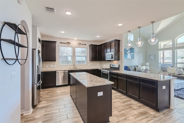 kitchen with sink, hanging light fixtures, stainless steel appliances, tasteful backsplash, and a kitchen island