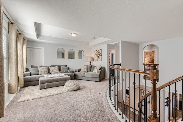 living room with a raised ceiling, light colored carpet, and a textured ceiling