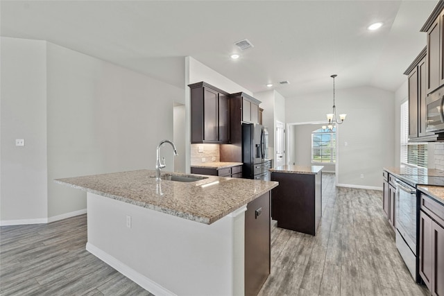 kitchen with light stone countertops, sink, an island with sink, stainless steel appliances, and lofted ceiling