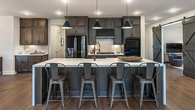 kitchen featuring tasteful backsplash, a barn door, light countertops, black appliances, and dark wood-type flooring