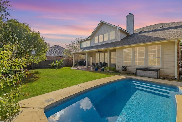 back house at dusk with ceiling fan, a patio area, and a yard