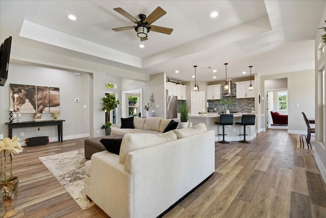 living room featuring ceiling fan, light hardwood / wood-style floors, and a raised ceiling