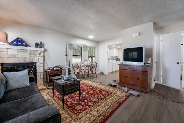 living room featuring a stone fireplace, hardwood / wood-style floors, and a textured ceiling