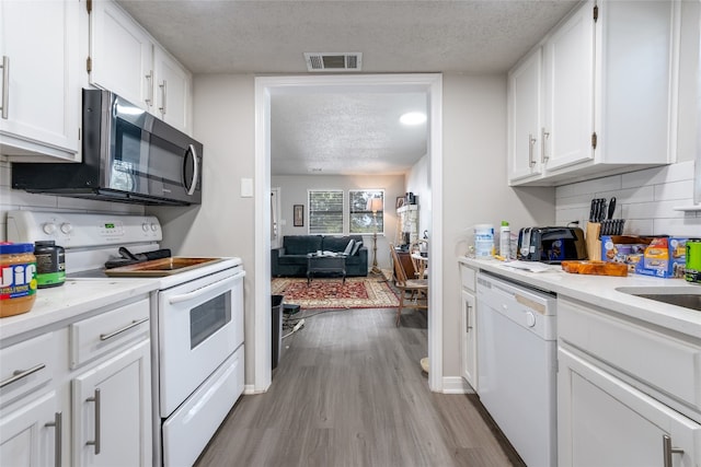 kitchen with white appliances, backsplash, a textured ceiling, light hardwood / wood-style floors, and white cabinets