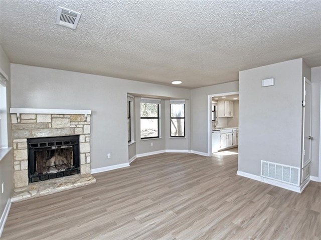21401 Patton Ave Unit A & B, Lago Vista, TX 78645 - unfurnished living room featuring light wood-type flooring, a textured ceiling, baseboards, and a stone fireplace