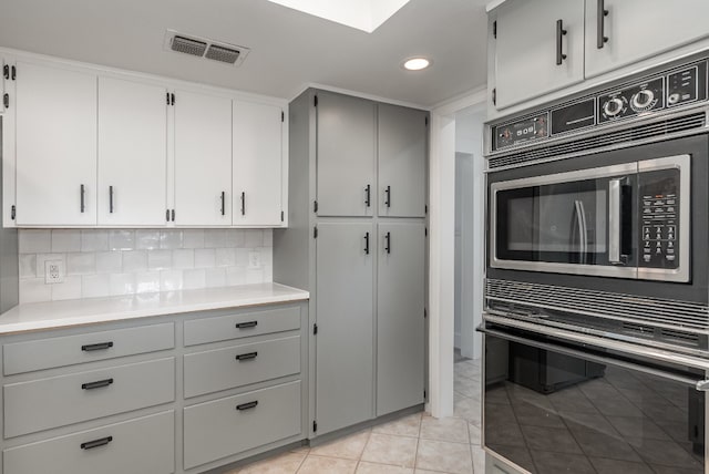 kitchen with oven, tasteful backsplash, light tile patterned floors, built in microwave, and gray cabinets