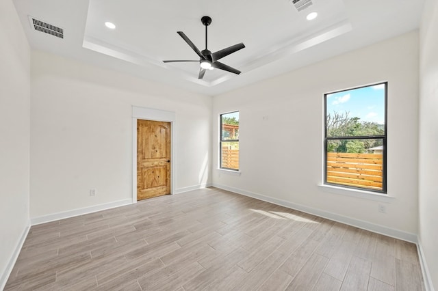 spare room with a tray ceiling, light wood-type flooring, and ceiling fan