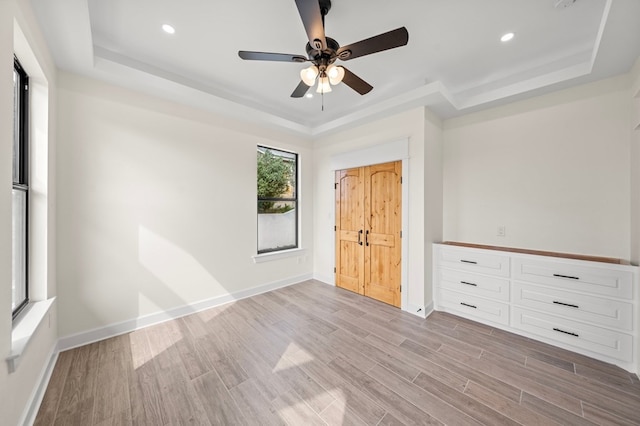 unfurnished bedroom with light hardwood / wood-style flooring, ceiling fan, and a raised ceiling