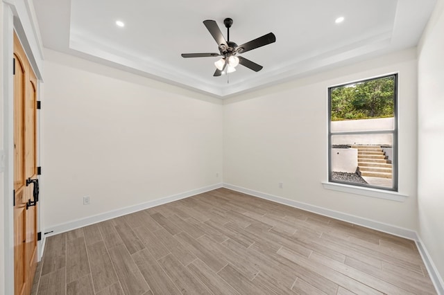 empty room featuring light hardwood / wood-style flooring, a tray ceiling, and ceiling fan