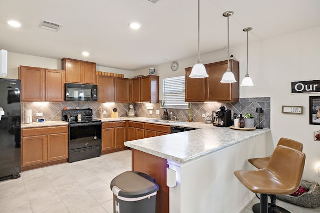 kitchen featuring black appliances, decorative light fixtures, kitchen peninsula, and a kitchen bar