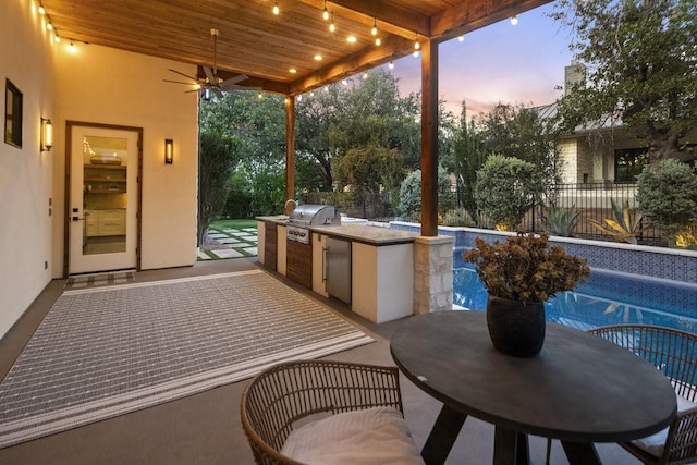 patio terrace at dusk featuring an outdoor kitchen, a fenced in pool, ceiling fan, and a grill