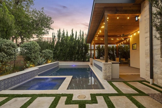 pool at dusk featuring a patio area, ceiling fan, and an in ground hot tub