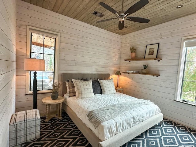 bedroom with ceiling fan, wooden ceiling, and wood walls