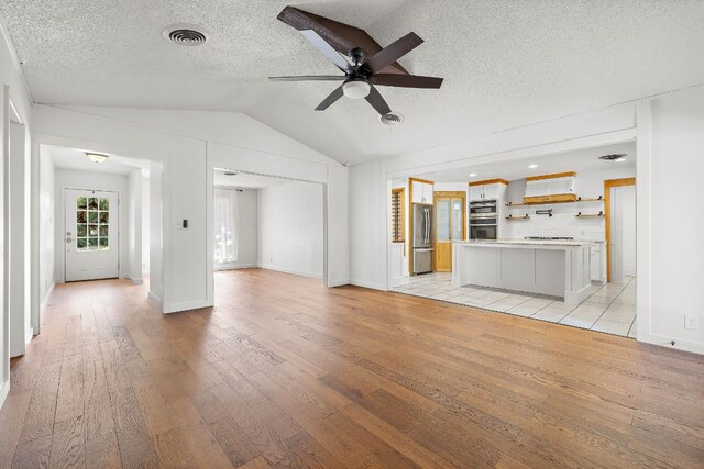 unfurnished living room featuring ceiling fan, light hardwood / wood-style floors, lofted ceiling, and a textured ceiling