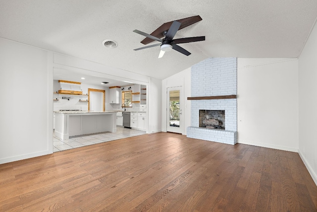 unfurnished living room featuring a fireplace, light hardwood / wood-style flooring, a textured ceiling, and vaulted ceiling