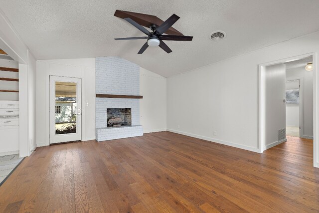 unfurnished living room featuring ceiling fan, a brick fireplace, hardwood / wood-style floors, a textured ceiling, and vaulted ceiling