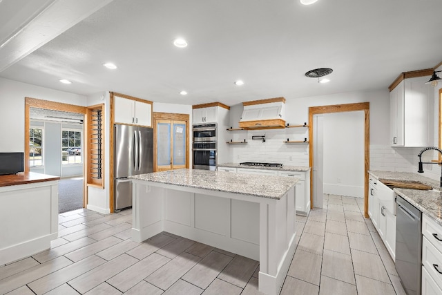 kitchen with decorative backsplash, appliances with stainless steel finishes, light stone counters, white cabinets, and a center island