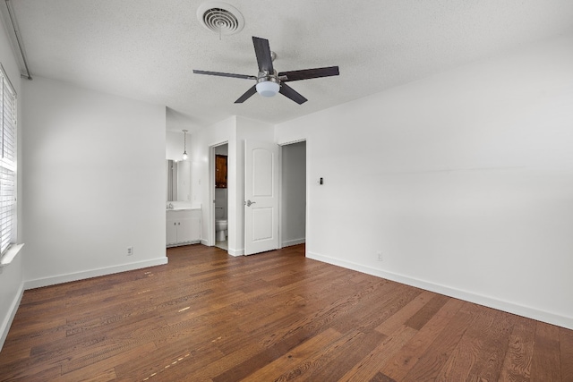 unfurnished bedroom with a textured ceiling, connected bathroom, dark hardwood / wood-style floors, and ceiling fan