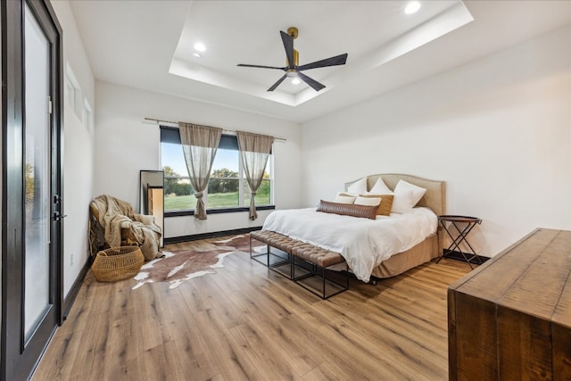 bedroom featuring ceiling fan, wood-type flooring, and a tray ceiling