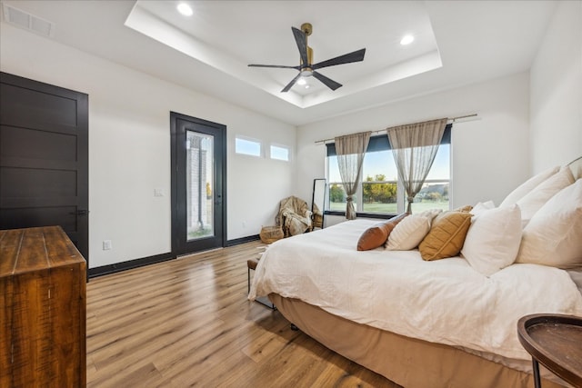 bedroom with a raised ceiling, access to exterior, light hardwood / wood-style floors, and ceiling fan