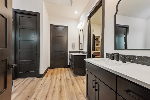 bathroom featuring two vanities, a closet, decorative backsplash, a sink, and wood finished floors