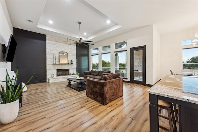 living room featuring light hardwood / wood-style floors, a tray ceiling, a fireplace, and ceiling fan