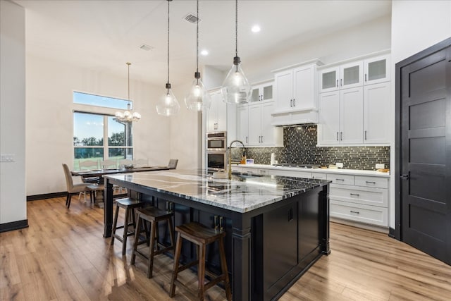 kitchen with white cabinetry, light hardwood / wood-style floors, hanging light fixtures, and a kitchen island with sink