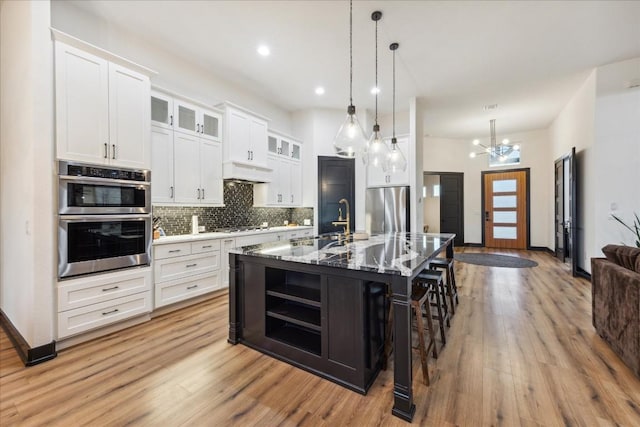 kitchen with light wood-style floors, a kitchen bar, tasteful backsplash, appliances with stainless steel finishes, and premium range hood