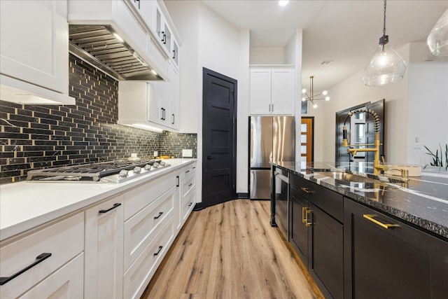 kitchen with hanging light fixtures, appliances with stainless steel finishes, premium range hood, white cabinetry, and light hardwood / wood-style flooring