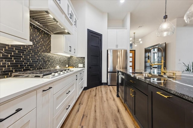 kitchen featuring white cabinets, appliances with stainless steel finishes, premium range hood, light wood finished floors, and backsplash
