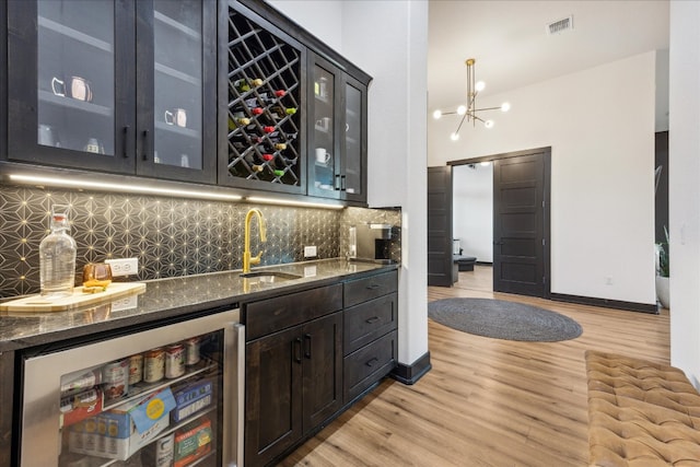 bar featuring dark stone counters, stainless steel fridge, sink, light wood-type flooring, and tasteful backsplash