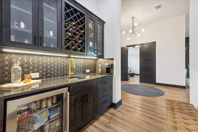bar with visible vents, wet bar, light wood finished floors, decorative backsplash, and beverage cooler