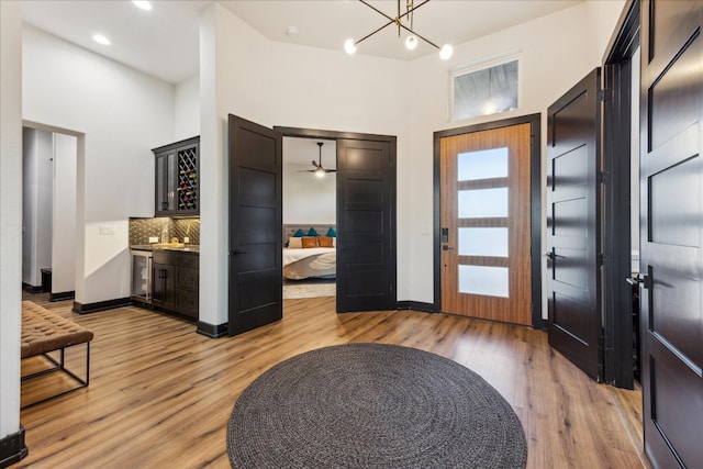 foyer with a towering ceiling, hardwood / wood-style floors, beverage cooler, and ceiling fan with notable chandelier