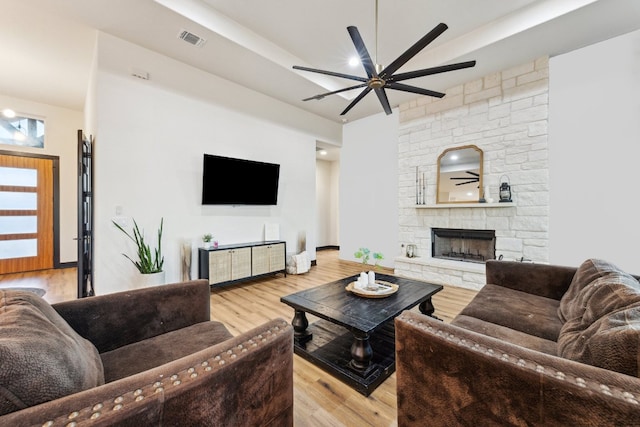 living area with wood finished floors, ceiling fan, a stone fireplace, and visible vents