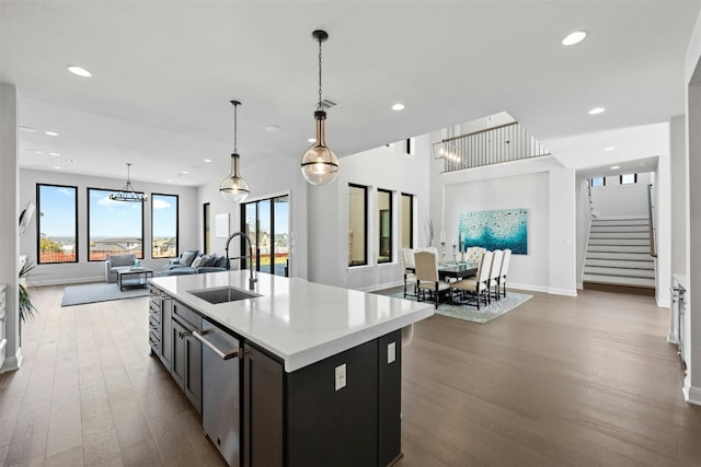 kitchen with sink, dark wood-type flooring, stainless steel dishwasher, decorative light fixtures, and a kitchen island with sink