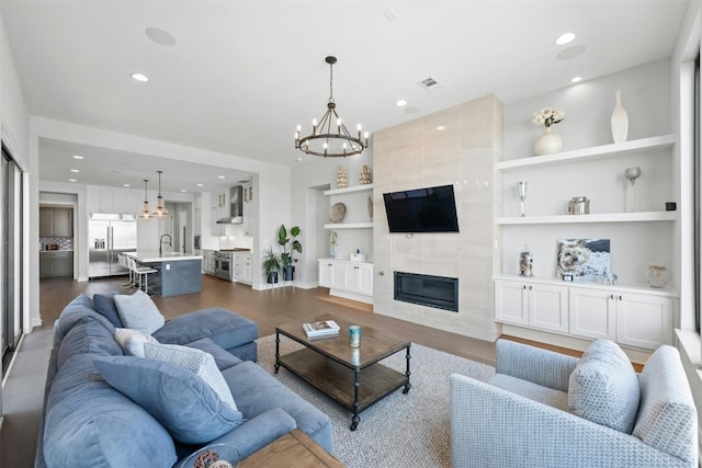 living room featuring dark hardwood / wood-style flooring, built in shelves, sink, an inviting chandelier, and a fireplace