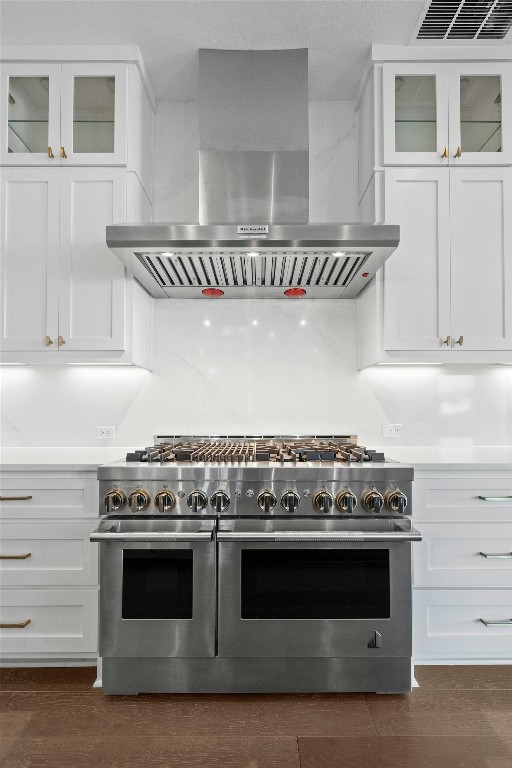 kitchen featuring wall chimney exhaust hood, dark hardwood / wood-style flooring, double oven range, and white cabinetry