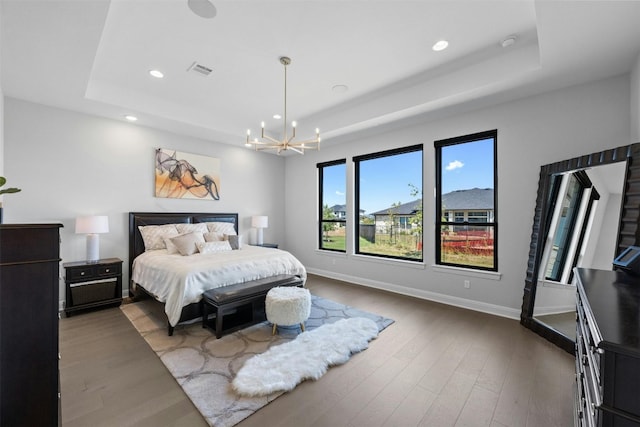 bedroom with dark hardwood / wood-style floors, an inviting chandelier, and a tray ceiling