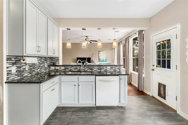 kitchen with a peninsula, white dishwasher, a sink, white cabinets, and tasteful backsplash