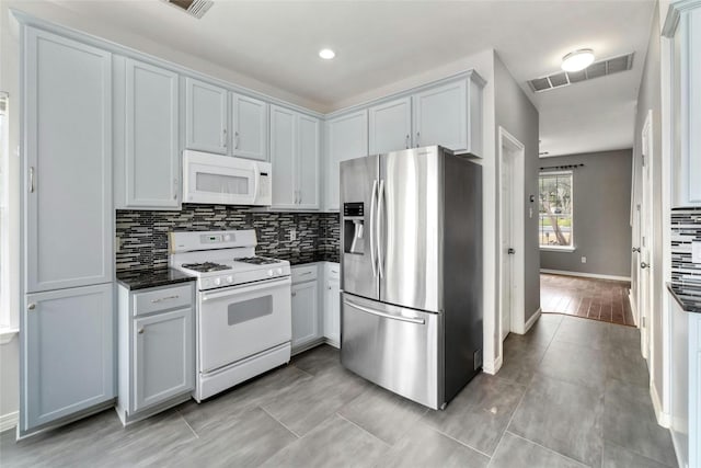 kitchen featuring tasteful backsplash, dark stone counters, light tile patterned flooring, and white appliances