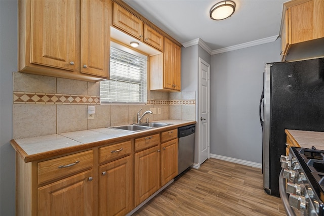 kitchen featuring appliances with stainless steel finishes, light wood-type flooring, ornamental molding, tile counters, and sink