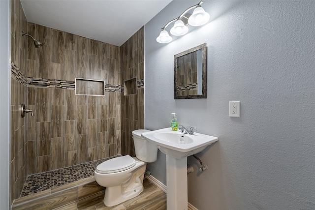 bathroom with hardwood / wood-style floors, a tile shower, and toilet