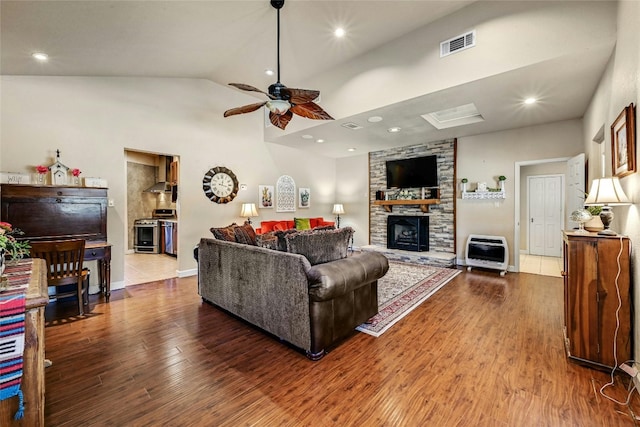 living room featuring a stone fireplace, hardwood / wood-style floors, heating unit, high vaulted ceiling, and ceiling fan