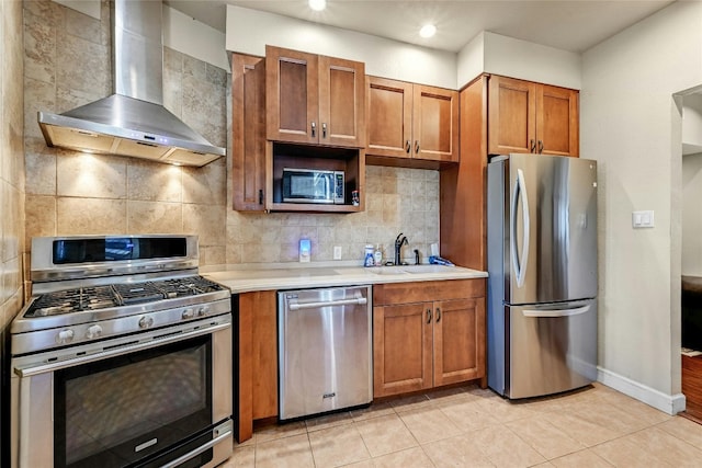 kitchen with wall chimney range hood, sink, stainless steel appliances, decorative backsplash, and light tile patterned floors