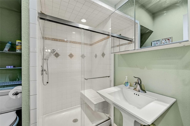 bathroom featuring a shower with door, toilet, and sink