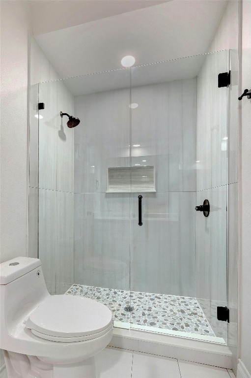 bathroom with a shower with door, toilet, and tile patterned flooring