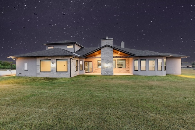 back house at night featuring a lawn