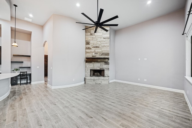 unfurnished living room featuring ceiling fan, light hardwood / wood-style floors, and a stone fireplace