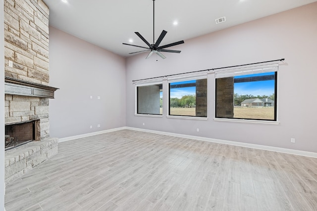 unfurnished living room with ceiling fan, a stone fireplace, and light hardwood / wood-style flooring