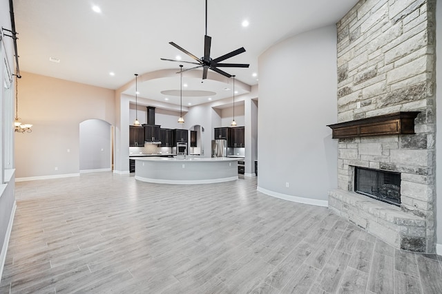 unfurnished living room with ceiling fan with notable chandelier, light hardwood / wood-style flooring, and a stone fireplace